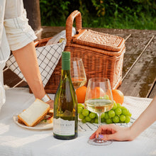 Load image into Gallery viewer, Picnic setup with a bottle of white wine, a glass, bread, and fruits on a blanket outdoors.