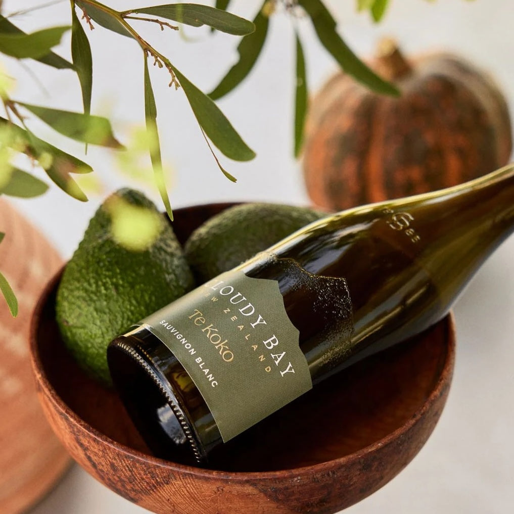 Load image into Gallery viewer, A bottle of white wine laying in a wooden bowl together with some avocados