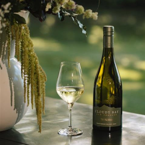 Load image into Gallery viewer, Bottle of Cloudy Bay Sauvignon Blanc with a glass of wine on a table outdoors.