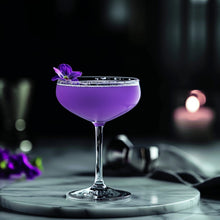 Load image into Gallery viewer, Purple cocktail in a glass with a flower on a dark background