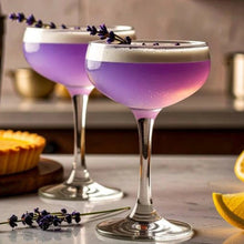 Load image into Gallery viewer, Two purple cocktails with a white foam top on a table with a pie and lemon slices.