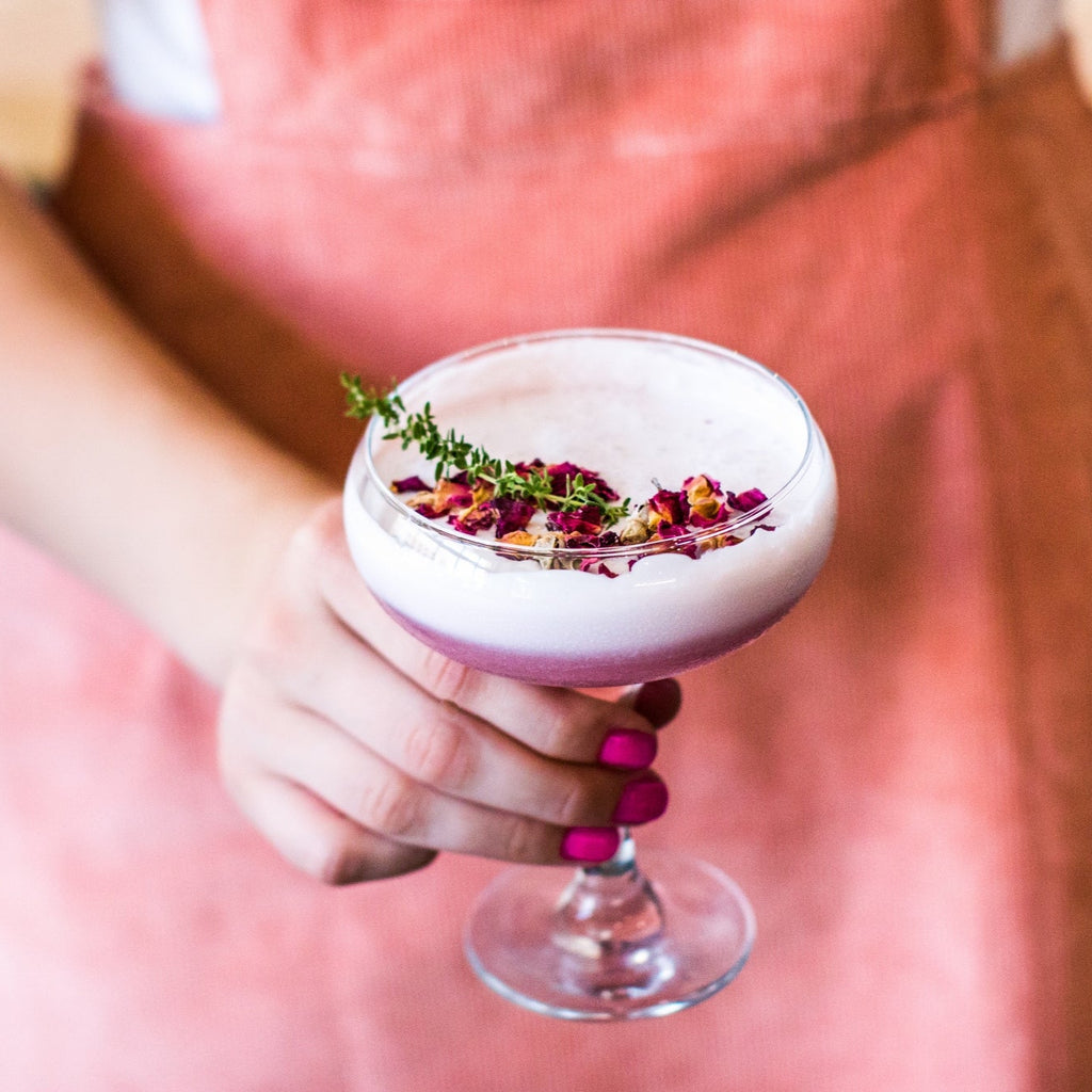 Person holding a pink cocktail with edible dried flower florets garnishes in a bar setting