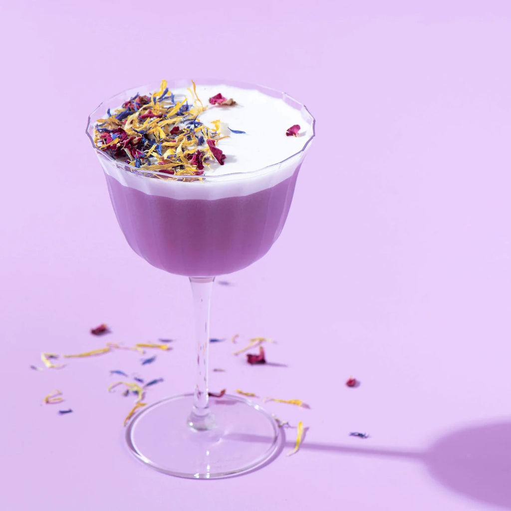 Stunning purple cocktail with beautiful edible dried florets as a garnish decoration on purple background