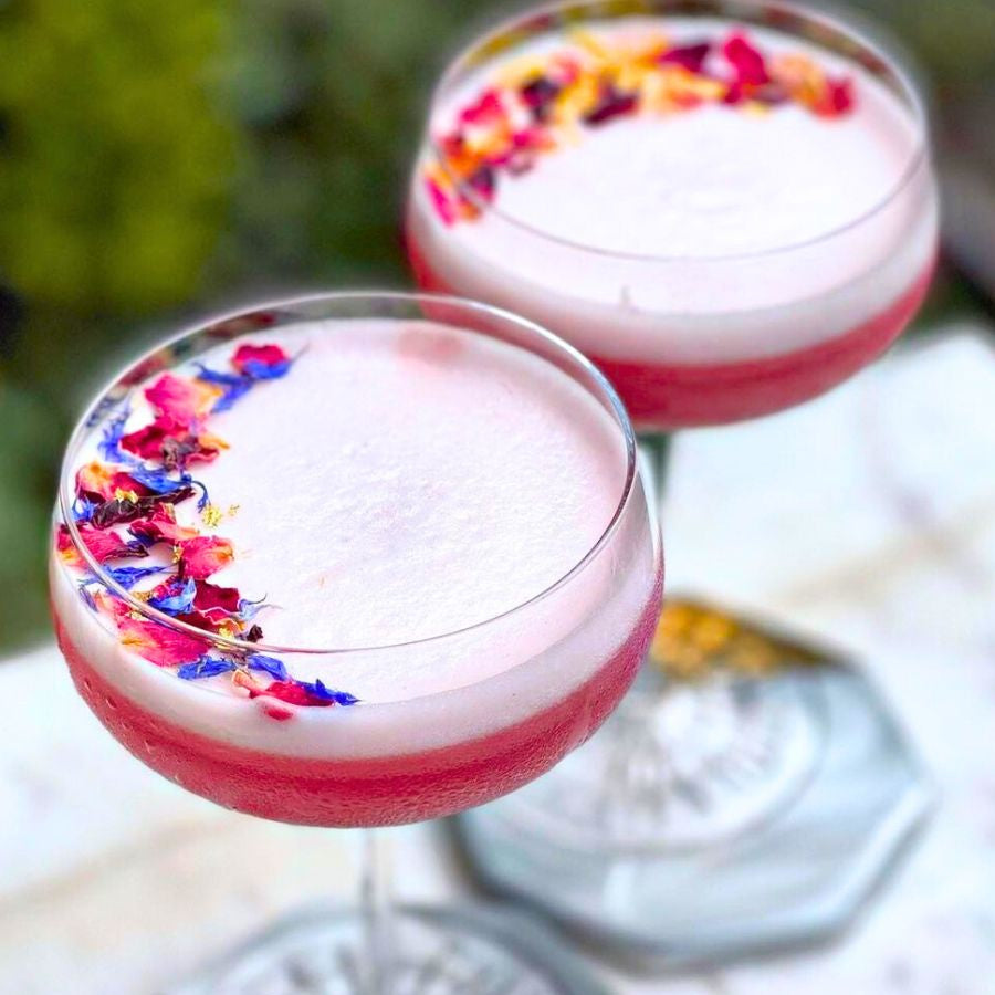 Load image into Gallery viewer, Two pink cocktails with edible dried floral petals on a white surface.