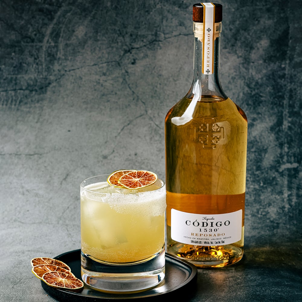 Load image into Gallery viewer, Bottle of Código reposado tequila with a cocktail on a dark surface