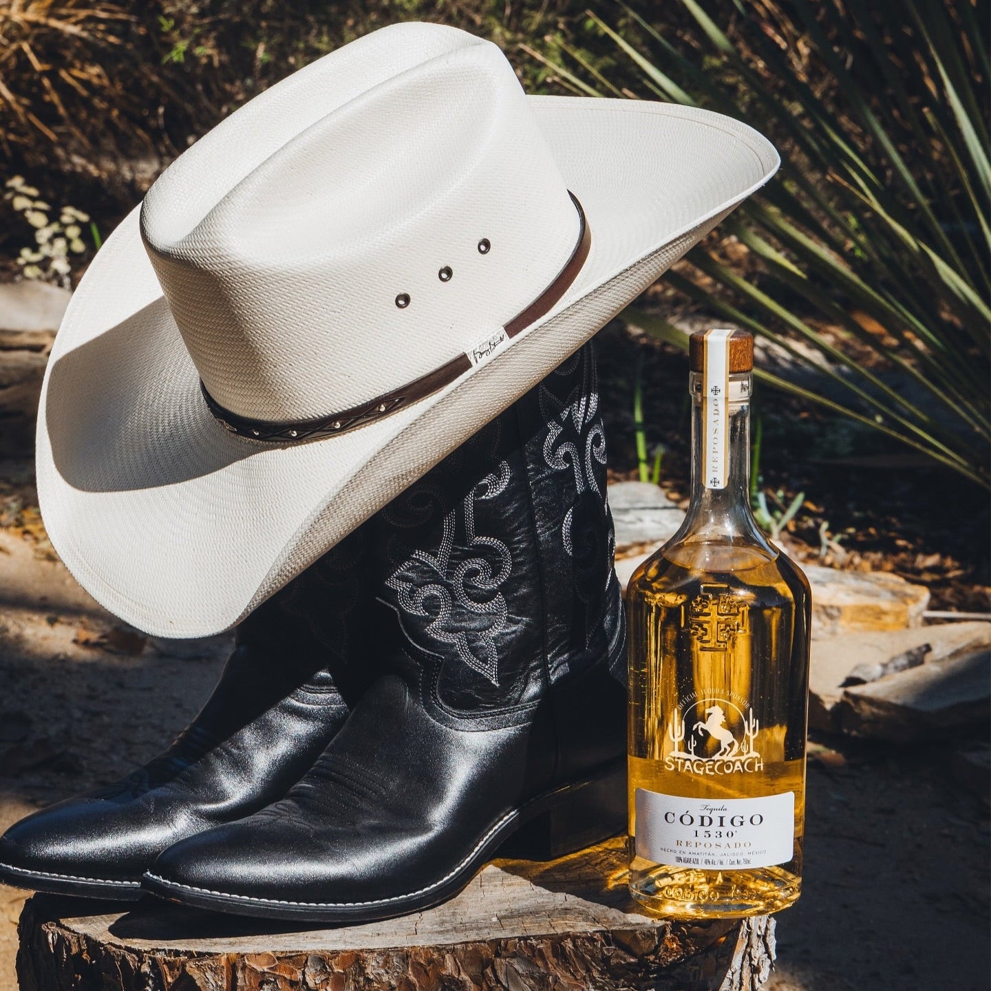 Load image into Gallery viewer, Cowboy hat and boots with a bottle of Código reposado tequila on a wooden surface.