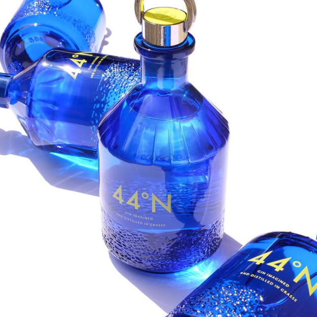 Load image into Gallery viewer, Three blue glass bottles of Comte de Grasse 44 degrees N Gin arranged diagonally on a white background with dramatic shadows.