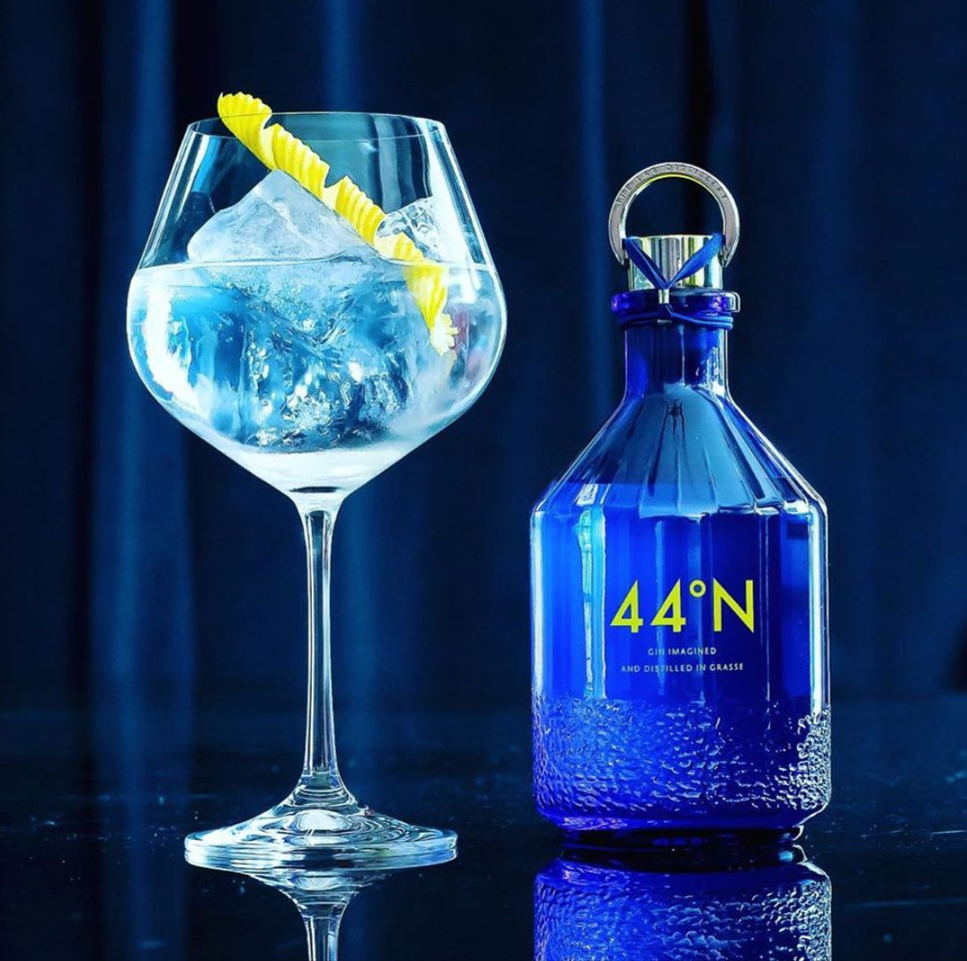 Load image into Gallery viewer, Blue bottle of Comte de Grasse 44 degrees N Gin with a cocktail in a glass on a dark background