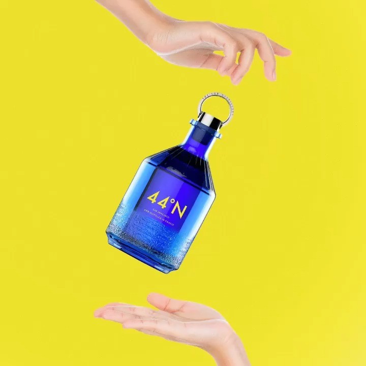 Blue bottle with '44 degrees N gin' label held by a hand against a yellow background