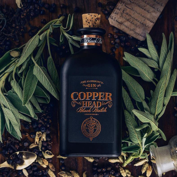 Load image into Gallery viewer, Bottle of Copperhead Black Batch Gin surrounded by herbs and spices on a wooden surface