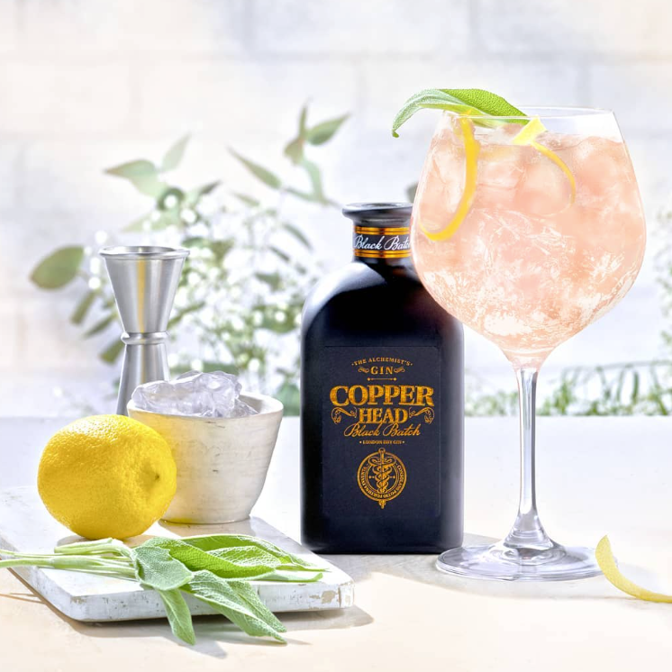 Load image into Gallery viewer, Copperhead Black Batch Gin bottle with a cocktail and garnishes on a blurred outdoor background