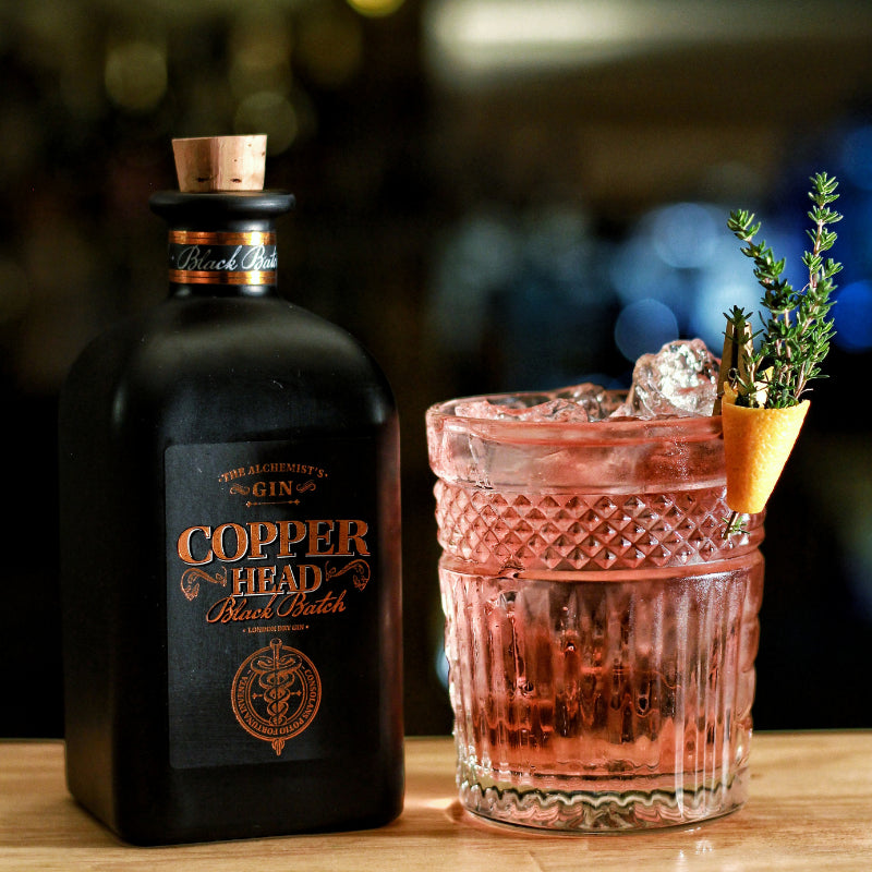Load image into Gallery viewer, Copperhead Black Batch Gin bottle with a cocktail garnished with a sprig of herbs on a wooden surface.