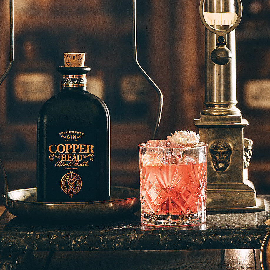 Load image into Gallery viewer, Copperhead Black Batch Gin bottle with a cocktail and flowers on a wooden table