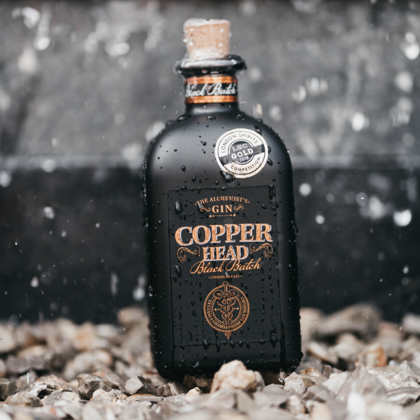 Load image into Gallery viewer, Copperhead Black Batch Gin bottle on pebbles in the rain