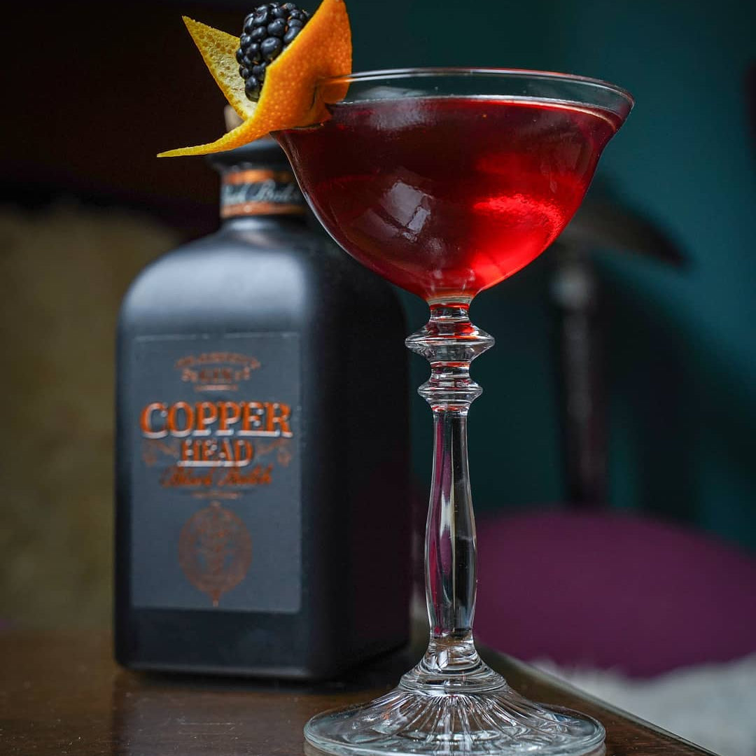 Load image into Gallery viewer, Red cocktail in a glass with a bottle of Copperhead Black Batch Gin in the background