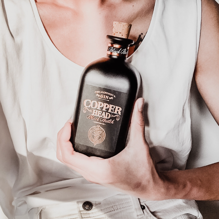 Load image into Gallery viewer, Woman holding a bottle of Copperhead Black Batch Gin with a white tank top and light pants.