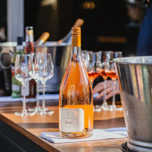 Load image into Gallery viewer, Bottle of Rosé wine on a bar counter with glasses and a person in the background.