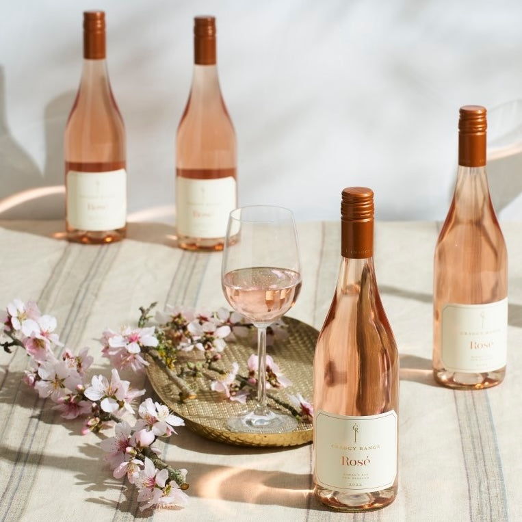 Load image into Gallery viewer, Bottles of Craggy Range Hawke's Bay Rosé and a wine glass with a full glass of rosé on a table with some blossoms as decorations
