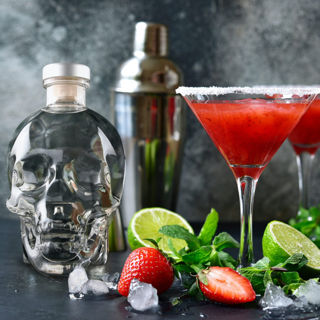 Two red cocktails in martini glasses with a Crystal Head Vodka bottle and cocktail shaker on a dark surface.