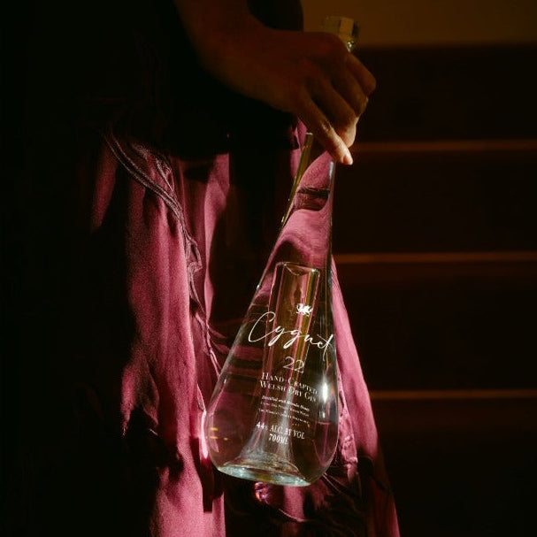 Load image into Gallery viewer, A woman in a dark pink dress holding a clear glass bottle of Cygnet 22 Welsh Dry Gin