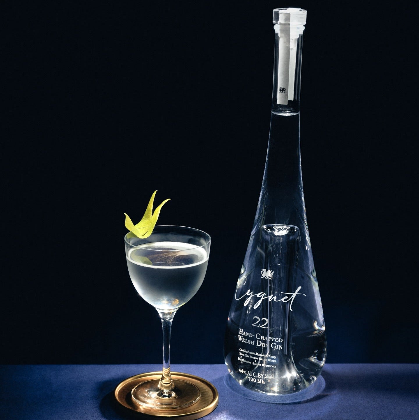 Load image into Gallery viewer, Bottle of Cygnet 22 Welsh Dry Gin and a cocktail glass with a lemon twist on a dark background