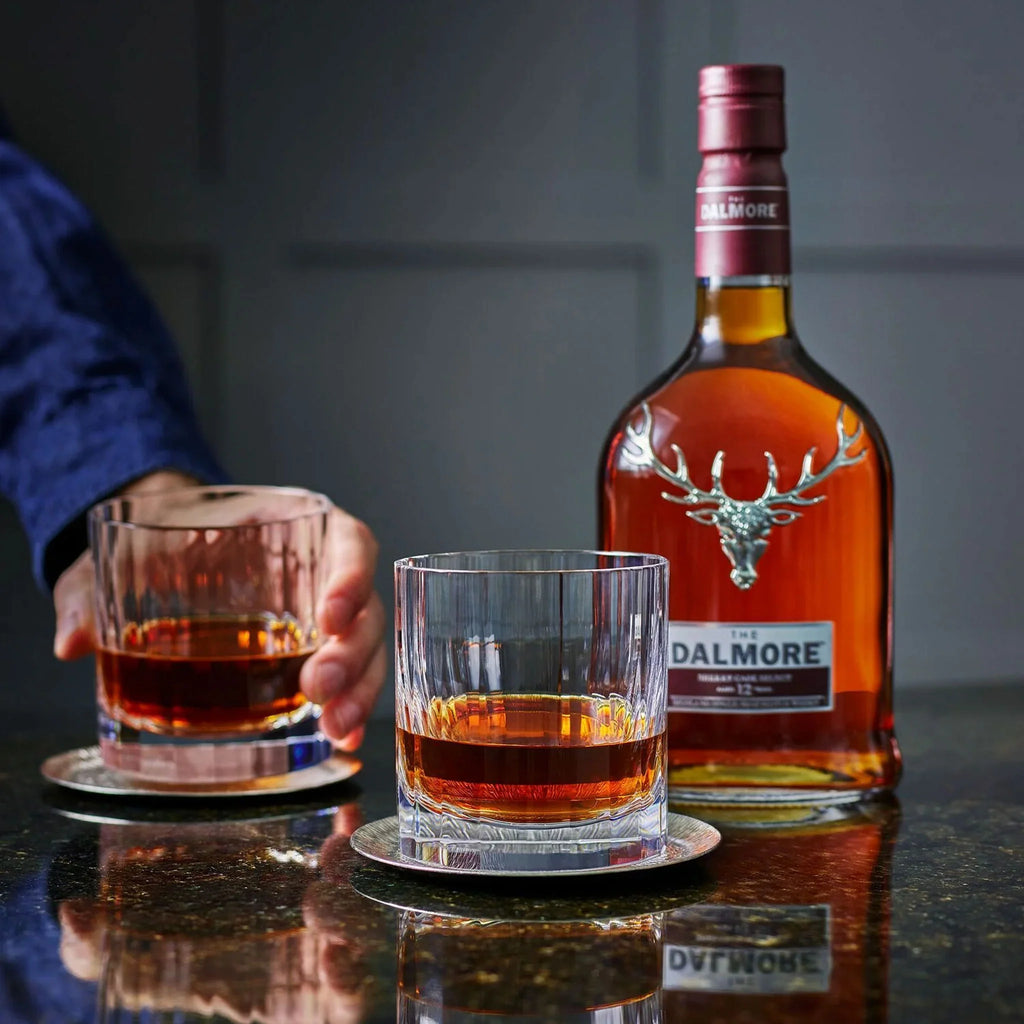 Two glasses of Dalmore whisky on coasters with a bottle of Dalmore whisky in the background.