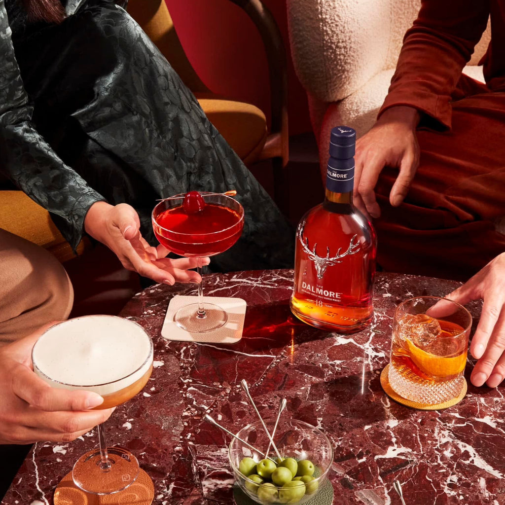 Two people enjoying cocktails at a table with a bottle of Dalmore 18 YEAR OLD 
whisky.