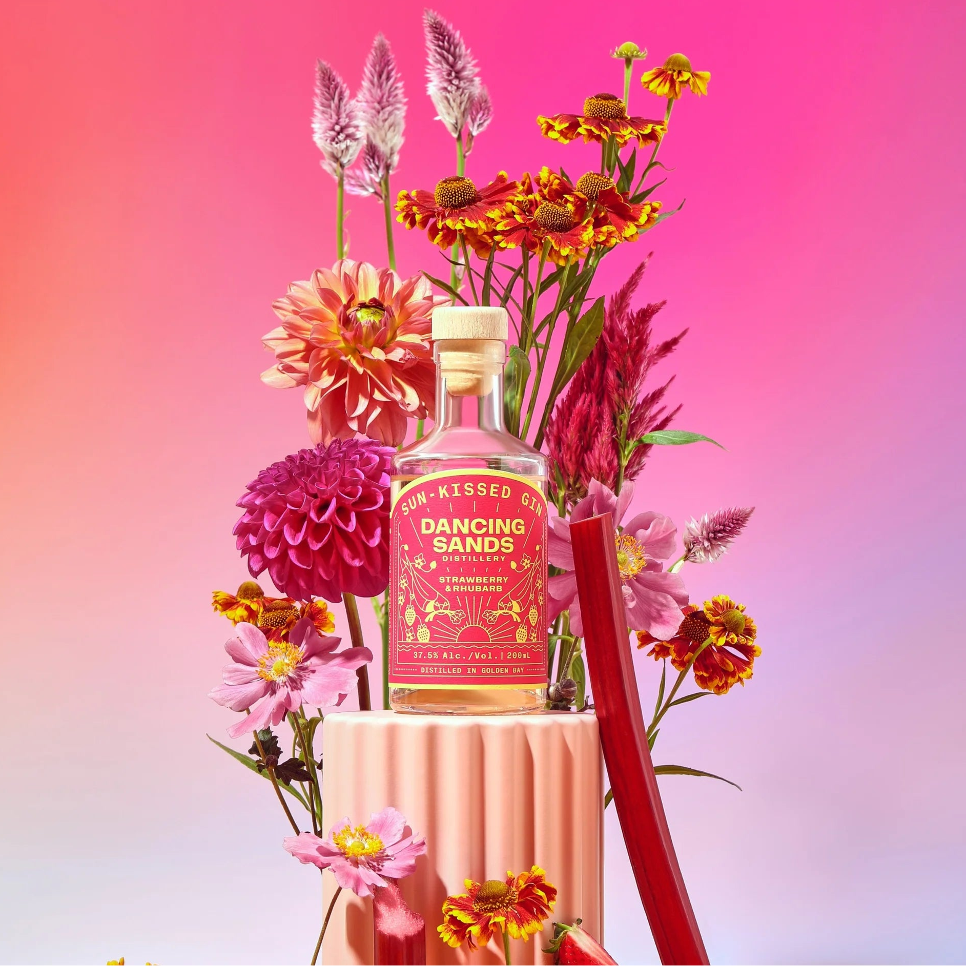 Load image into Gallery viewer, Bottle of 'Dancing Sands' gin surrounded by colorful flowers on a pink and purple gradient background