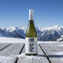 Load image into Gallery viewer, Bottle of sake on a wooden platform with snow-covered mountains in the background