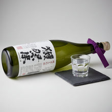 Load image into Gallery viewer, Green bottle of Japanese sake with a purple ribbon next to a shot glass on a gray background