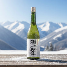Load image into Gallery viewer, Japanese Sake bottle with a label on a wooden surface against a snowy mountain backdrop