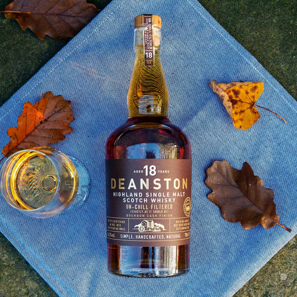 Deanston 18 year old whisky bottle with a glass on a blue cloth with autumn leaves