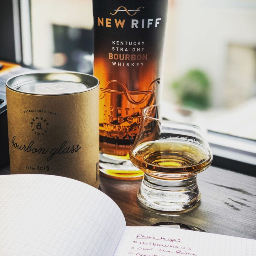 Load image into Gallery viewer, New Riff Kentucky Straight Bourbon Whiskey bottle next to a Denver and Liely Bourbon Glass glass with whiskey on a table next to a notebook.