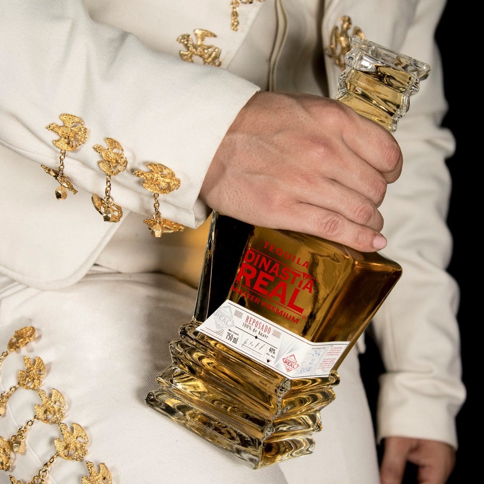 Load image into Gallery viewer, A Mexican man in traditional costume holding a bottle of Dinastia Real Master Premium Reposado Tequila