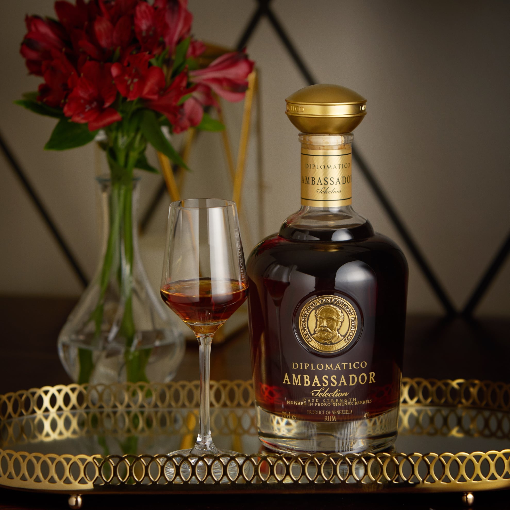 Load image into Gallery viewer, Bottle of Diplomatico Ambassador Selection Rum with a glass on a decorative table.