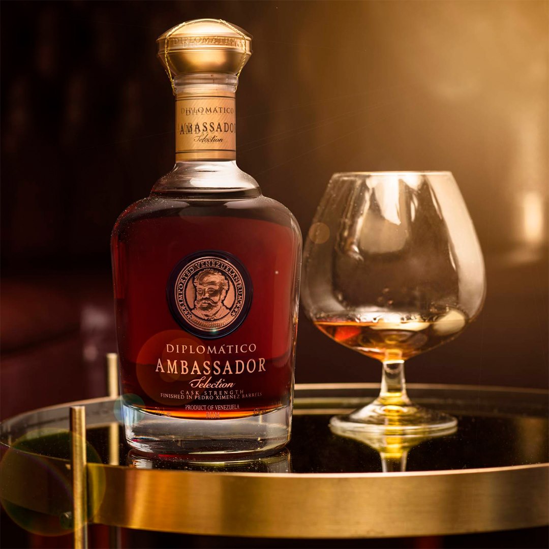 Load image into Gallery viewer, Bottle of Diplomatico Ambassador Selection Rum with a glass on a reflective surface