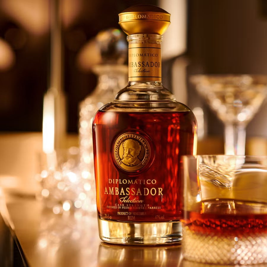 Load image into Gallery viewer, Bottle of Diplomatico Ambassador Selection Rum on a bar with glasses in the background