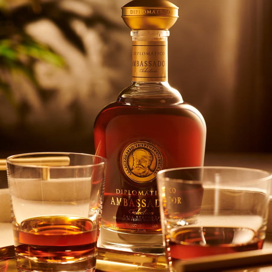 Load image into Gallery viewer, Bottle of Diplomatico Ambassador Selection Rum with two glasses on a reflective surface.