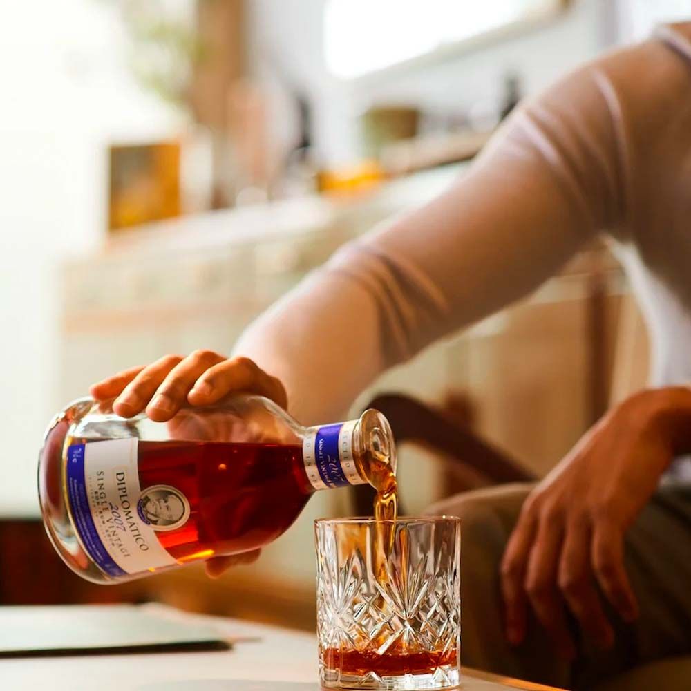 Man pouring a drink from a bottle into a glass on a table.
