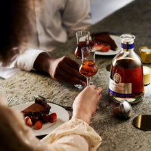 Load image into Gallery viewer, Two people enjoying dessert and drinks at a bar with a bottle of Kahlua in the foreground.