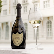 Load image into Gallery viewer, Dom Perignon champagne bottle and glass with a blurred building background