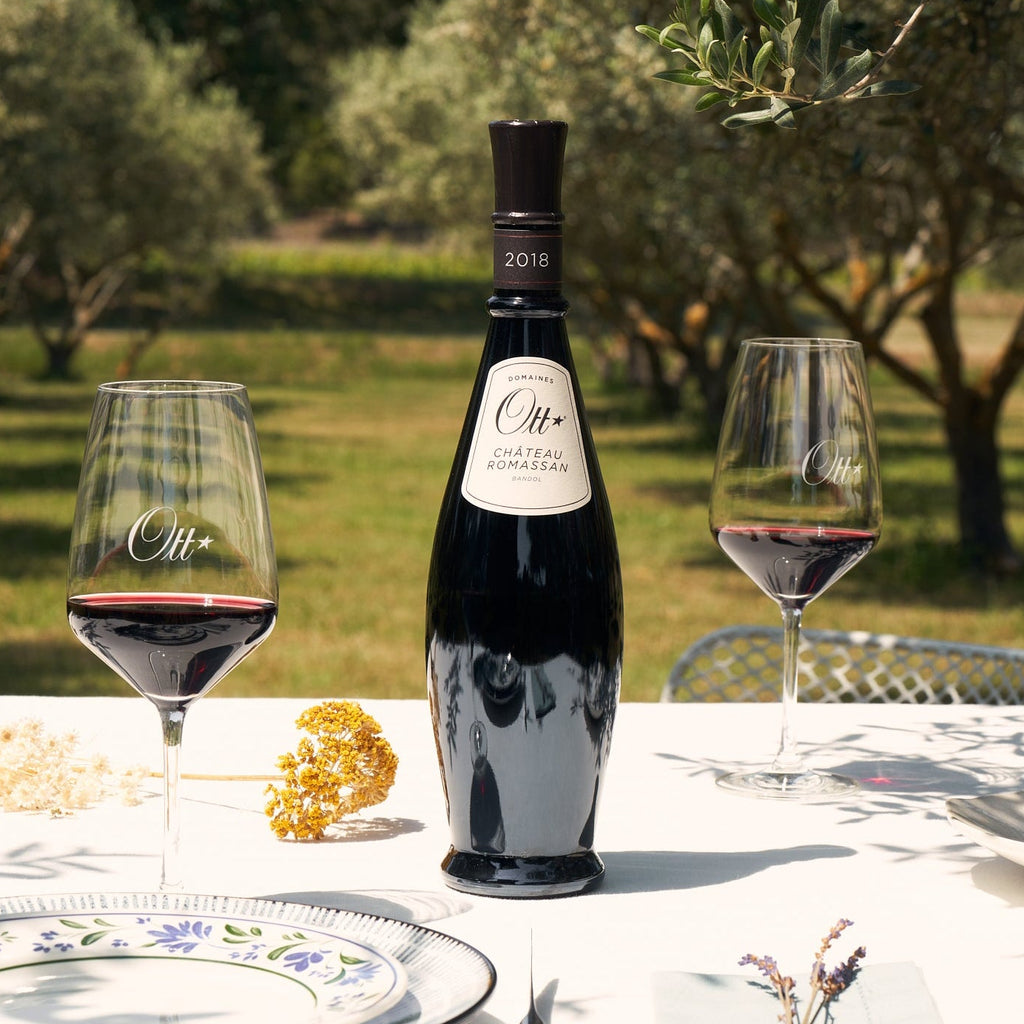 Domaines Ott Chateau Romassan Bandol Rouge red wine bottle and glasses on a table with an olive grove in the background