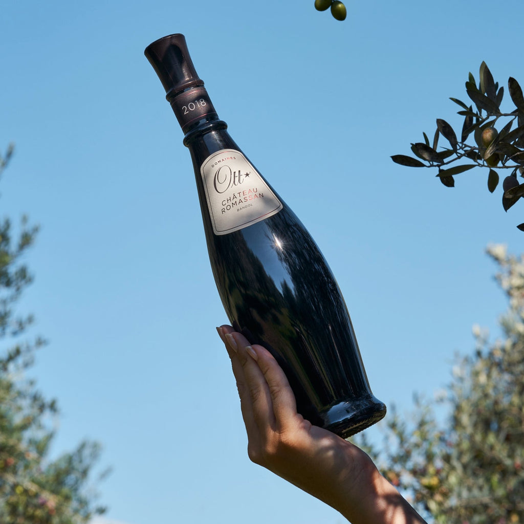 Bottle of Domaines Ott Chateau Romassan Bandol Rouge red wine held by a hand with a clear blue sky and olive trees in the background
