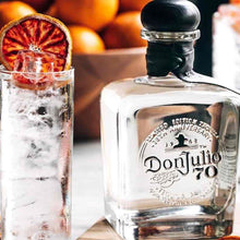 Load image into Gallery viewer, Don Julio 70 tequila bottle with a cocktail garnished with dried fruit on a table.