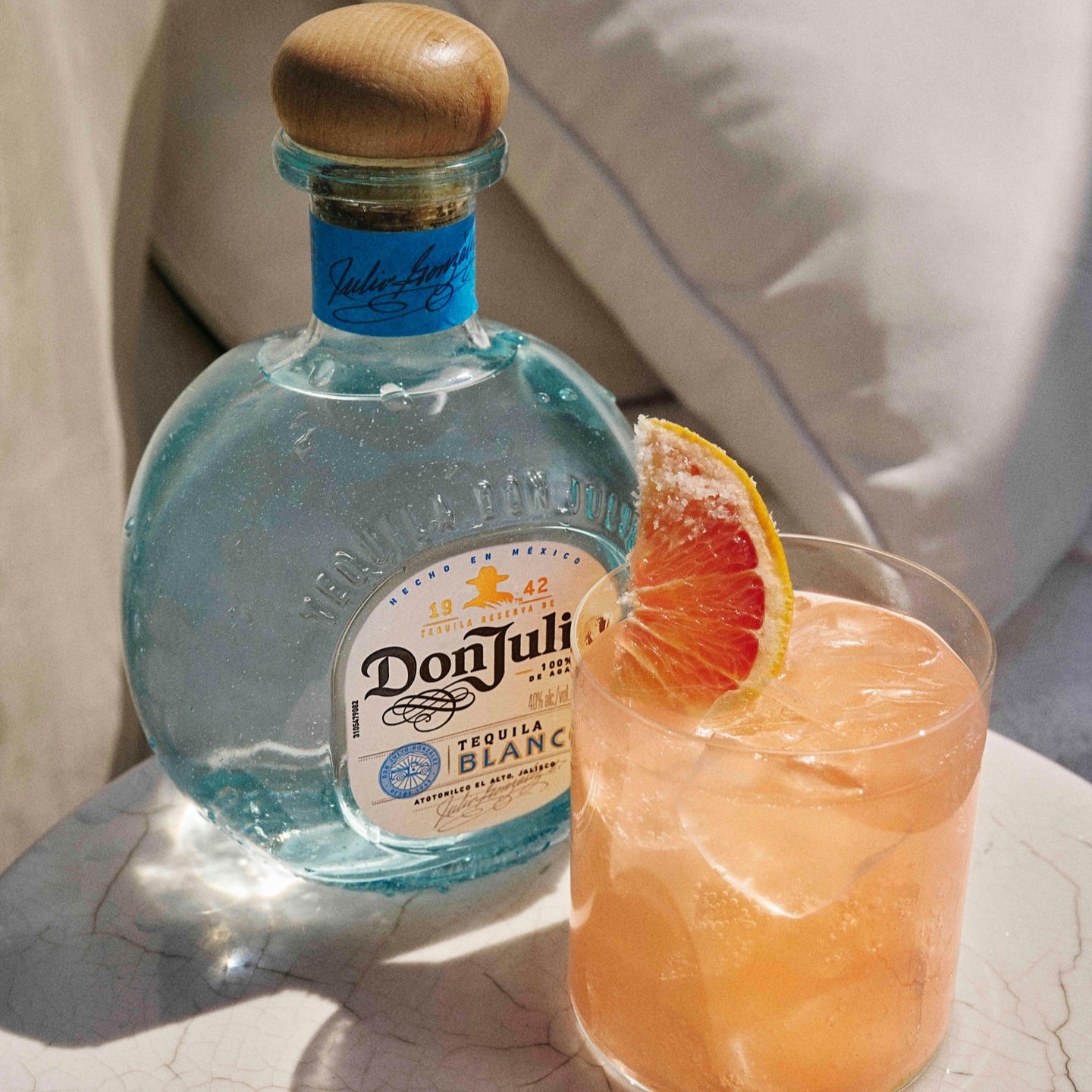Load image into Gallery viewer, Bottle of Don Julio Blanco Tequila with a cocktail garnished with a grapefruit slice on a light surface.