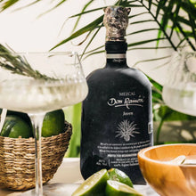 Load image into Gallery viewer, Bottle of Don Ramon Mezcal with limes and a glass on a table with greenery in the background
