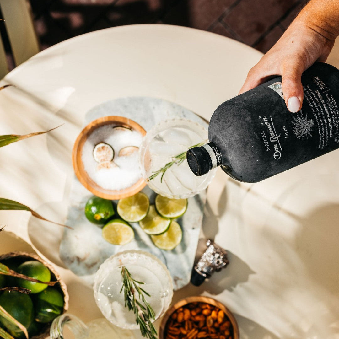 Load image into Gallery viewer, Person pouring a drink into a glass with ice and limes on a table.