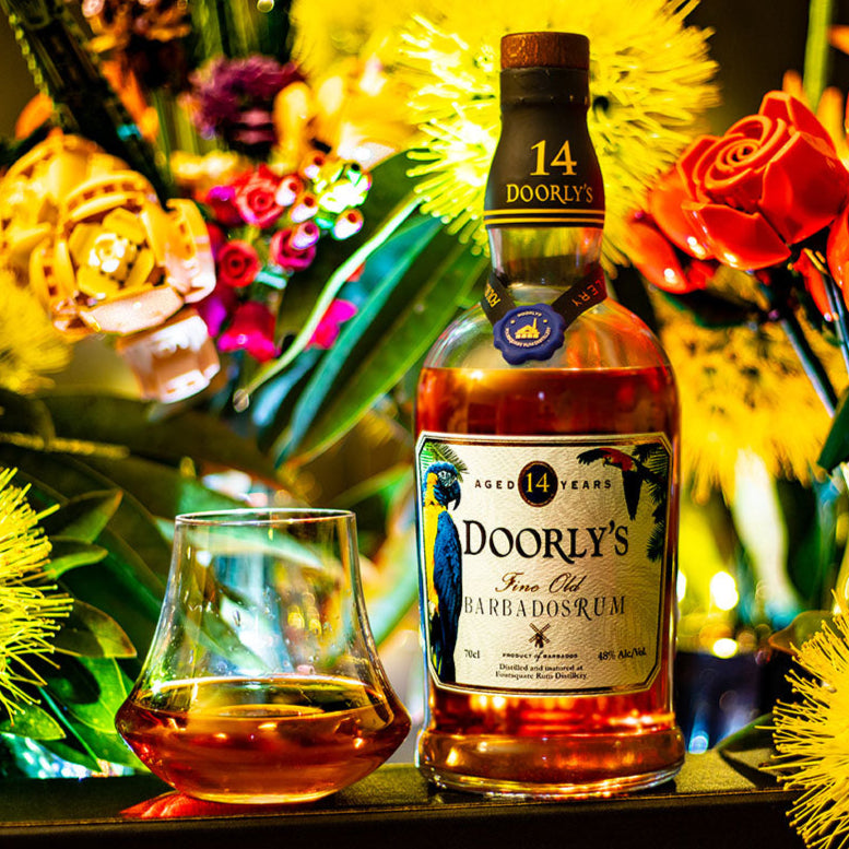 Load image into Gallery viewer, Bottle of Dooley's 14 YEAR OLD rum with a glass on a table surrounded by flowers