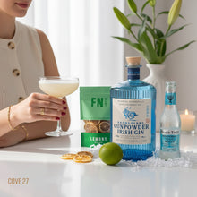 Load image into Gallery viewer, Woman holding a cocktail with Drumshanbo Gunpowder Irish Gin and a pouch of FN Lemons dried lemons Fever-Tree tonic water on a table.