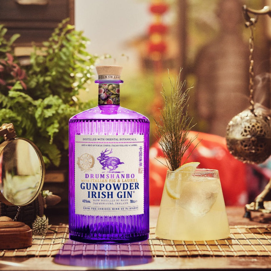 Load image into Gallery viewer, Purple bottle of Drumshanbo Gunpowder Irish Gin with a glass of lemonade on a decorative table.
